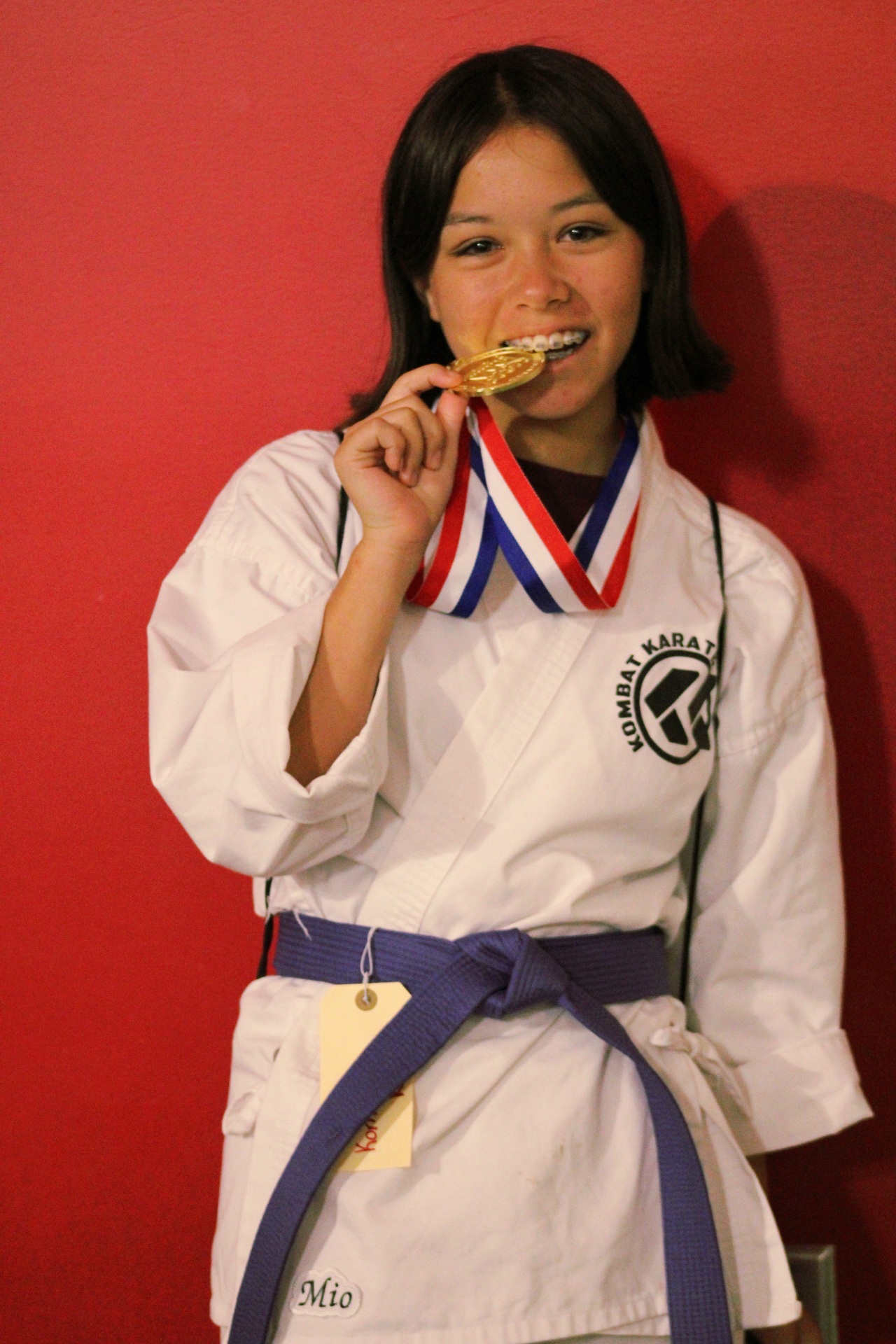 Teen Kombat Karate student biting her gold tournament medal in Long Beach, CA