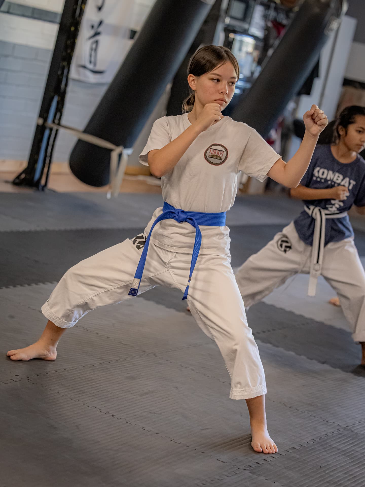 Teen student in a white gi with blue belt holding a front stance and guard during Shotokan karate class at Kombat Karate Long Beach