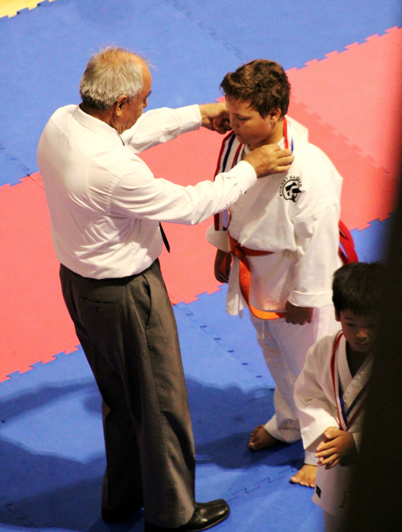 Young Kombat Karate student receiving a tournament medal on the competition mat