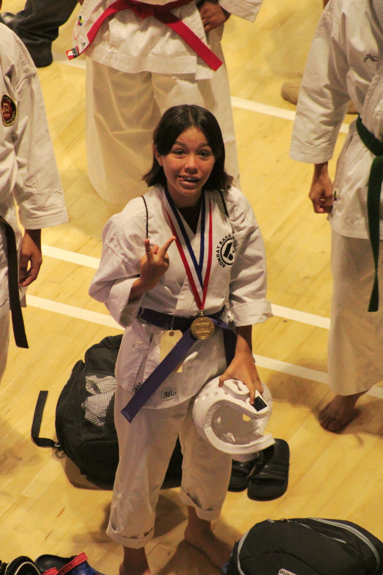 Teen karate competitor with her gold medal and sparring gear at a tournament